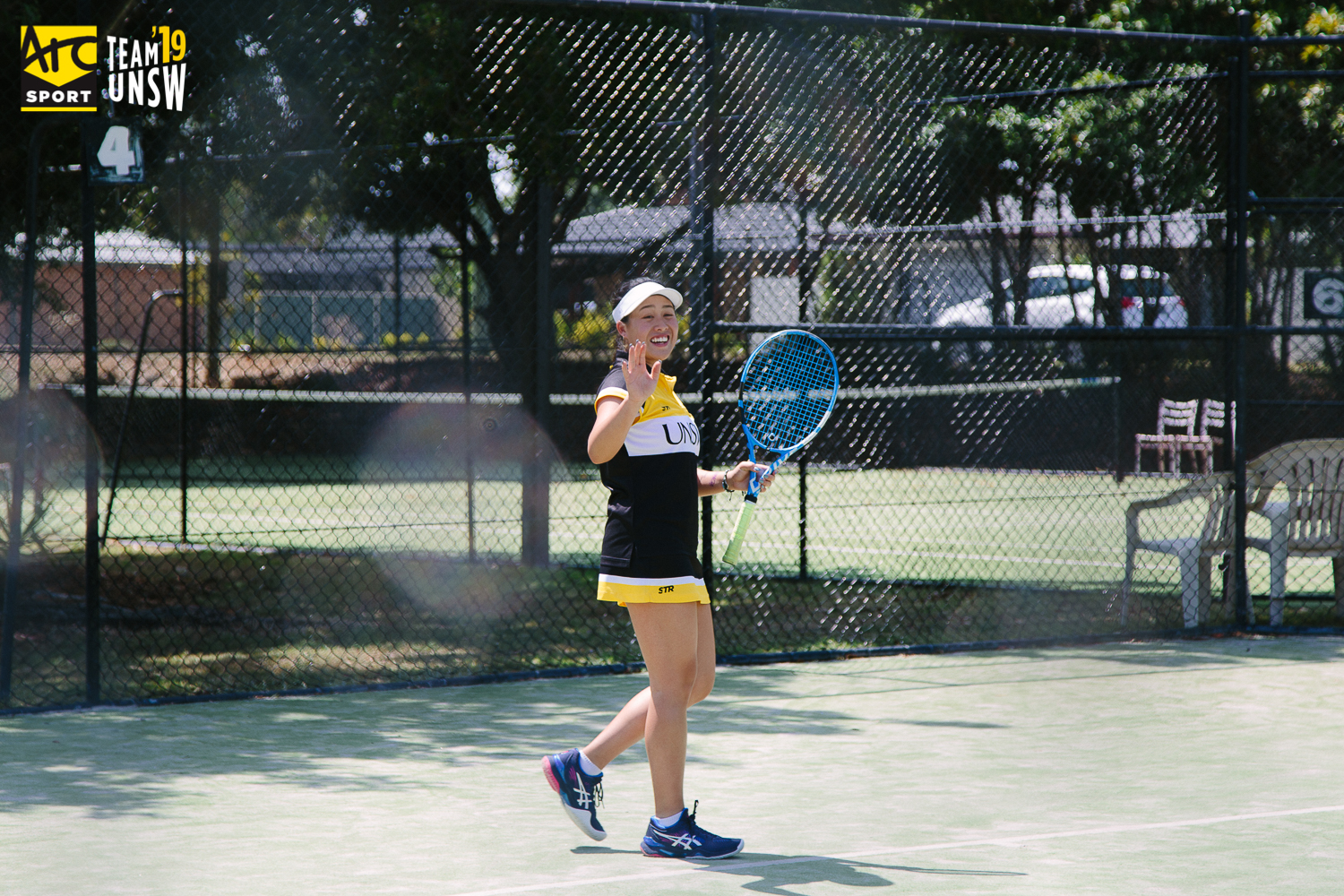 Student in UNSW tennis uniform waving at the camera